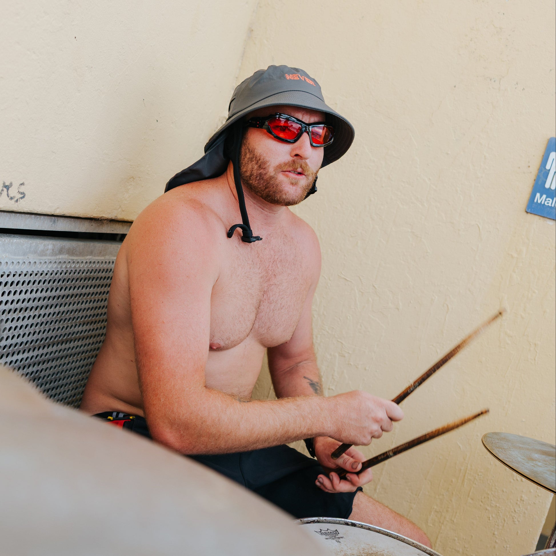 Wearing Plow Surf Hat in NEVER forget protection Charcoal colour. Man playing drums indoors with a neutral background