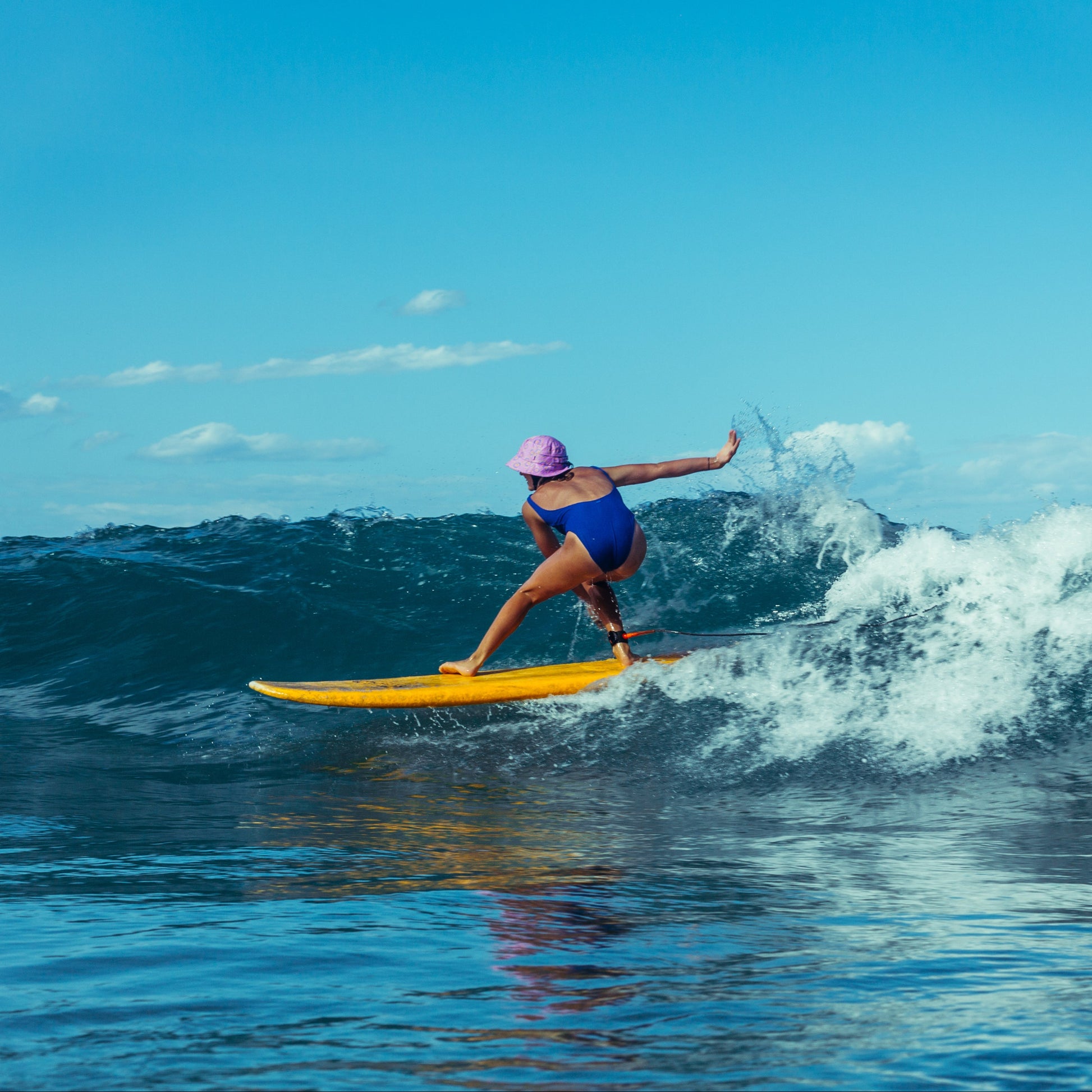 Leihani Zoric minishakas surfing on a wave with clear blue sky in her own plow surf co. surf hat design 